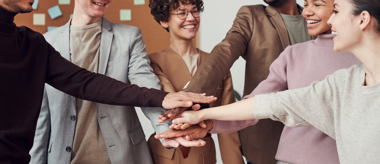 Services-01 A group of happy, diverse colleagues celebrating teamwork and cooperation with a group high five indoors.