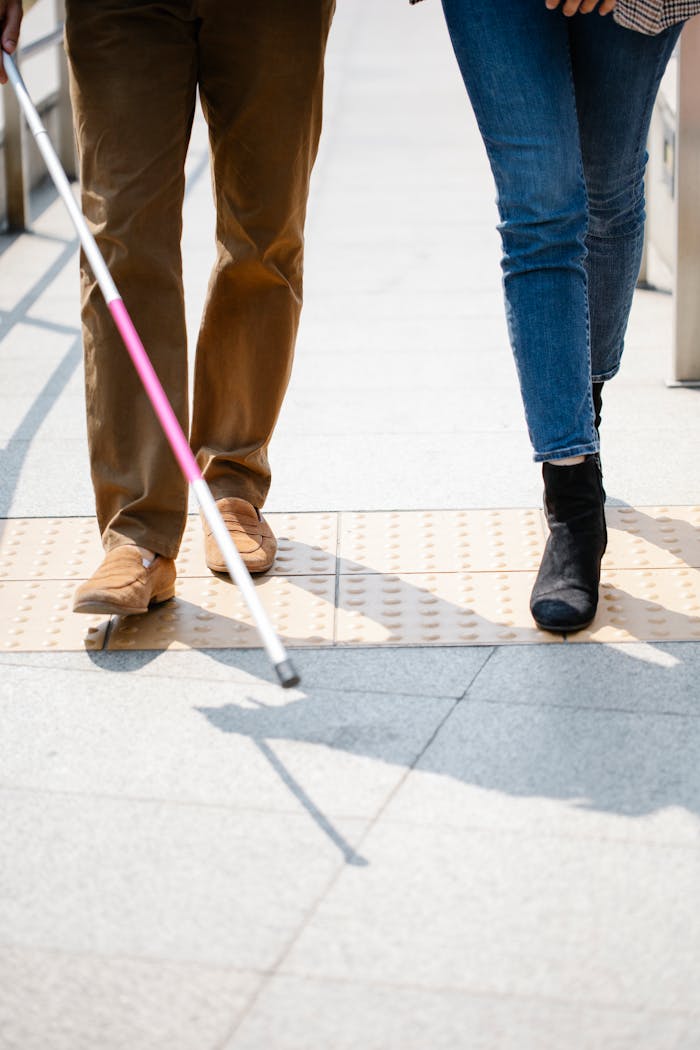 creative-02 Two individuals walking side by side, one using a white cane for guidance.