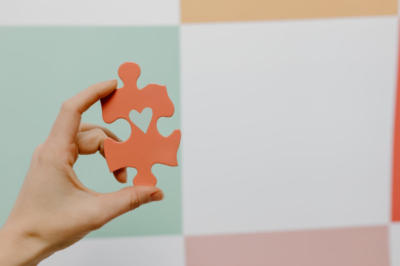 creative Close-up of a hand holding a heart-shaped puzzle piece against a colorful background.